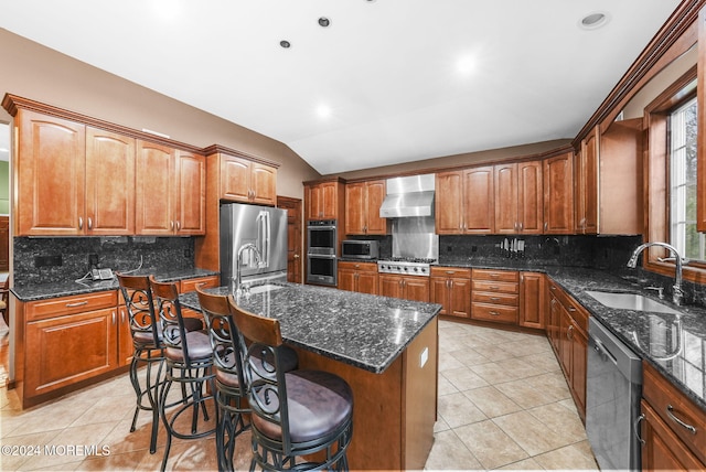 kitchen with a kitchen island with sink, sink, vaulted ceiling, wall chimney exhaust hood, and stainless steel appliances