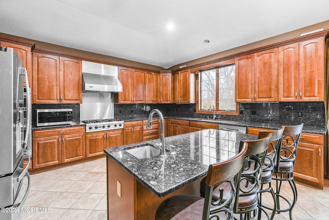 kitchen featuring sink, stainless steel appliances, wall chimney range hood, a breakfast bar area, and a center island with sink