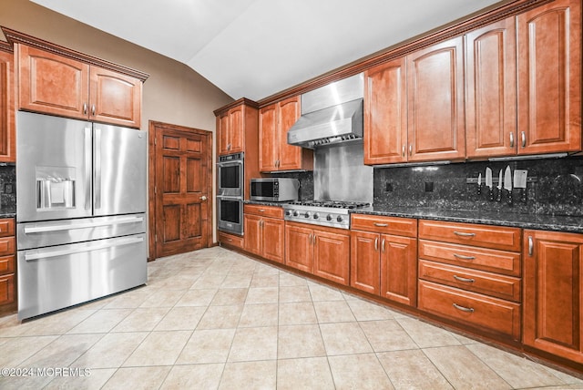 kitchen with dark stone counters, vaulted ceiling, wall chimney exhaust hood, tasteful backsplash, and stainless steel appliances