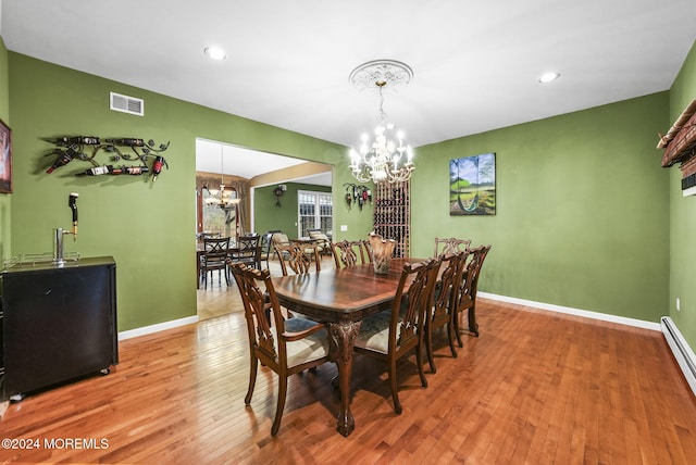 dining area with baseboard heating, hardwood / wood-style flooring, and a notable chandelier