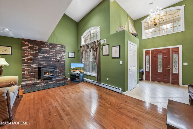 entrance foyer with baseboard heating, high vaulted ceiling, a chandelier, light hardwood / wood-style floors, and a wood stove