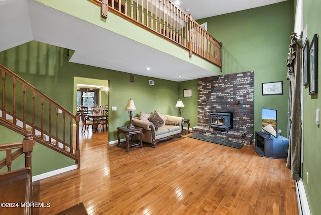 living room with wood-type flooring, a wood stove, baseboard heating, and a towering ceiling