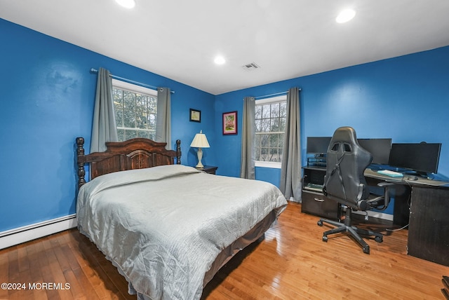 bedroom featuring wood-type flooring, a baseboard radiator, and multiple windows