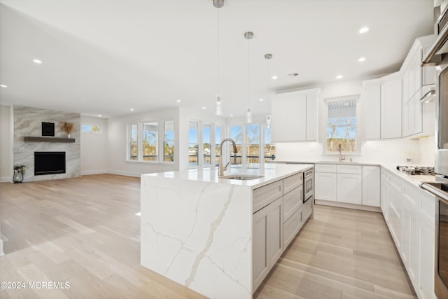 kitchen with a wealth of natural light, a kitchen island with sink, sink, and pendant lighting