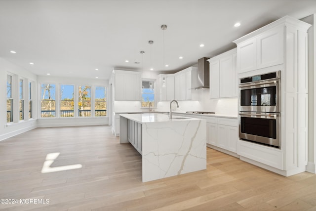 kitchen with a center island with sink, wall chimney exhaust hood, white cabinets, and stainless steel double oven