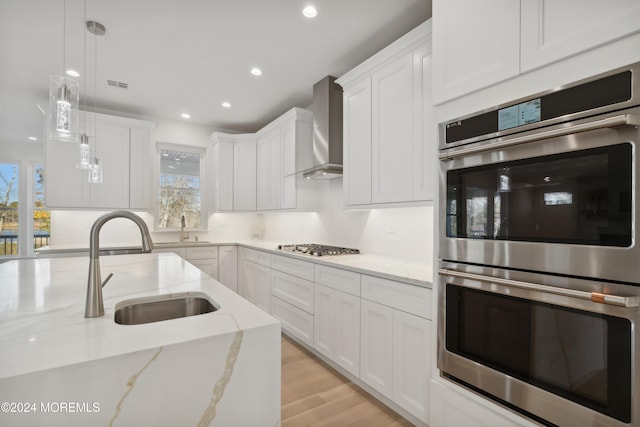 kitchen with pendant lighting, plenty of natural light, wall chimney range hood, and stainless steel appliances