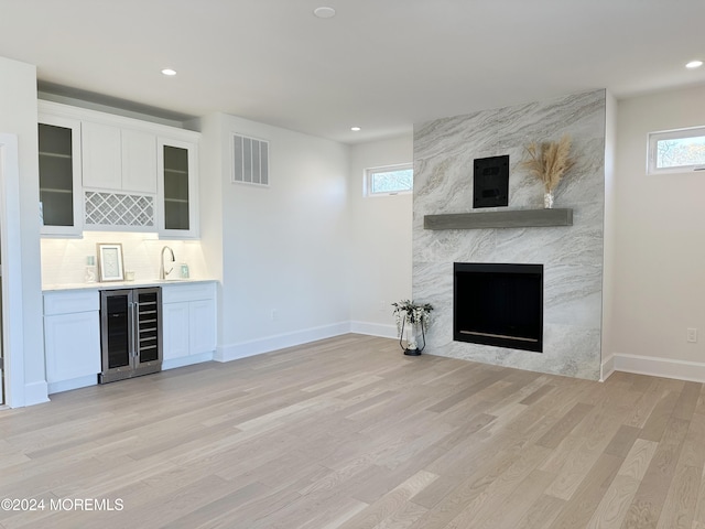 unfurnished living room with wine cooler, light hardwood / wood-style flooring, a healthy amount of sunlight, and wet bar