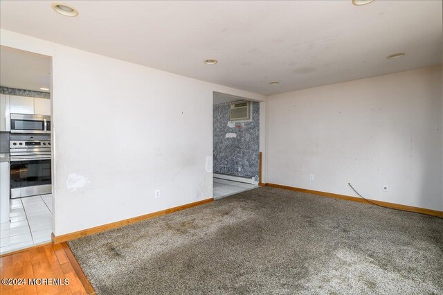 unfurnished room with baseboard heating, a wall mounted AC, and light hardwood / wood-style flooring