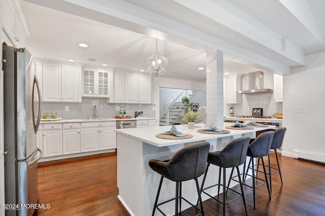 kitchen with wall chimney range hood, appliances with stainless steel finishes, a center island with sink, and white cabinets