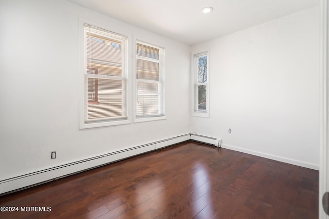 empty room featuring a baseboard heating unit, plenty of natural light, and hardwood / wood-style flooring