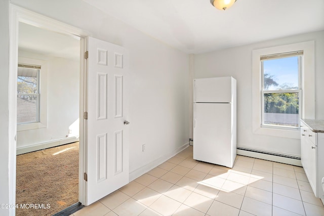 unfurnished bedroom with multiple windows, baseboard heating, and white fridge