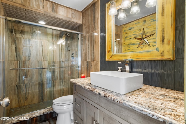 bathroom with vanity, toilet, a shower with door, and wooden walls