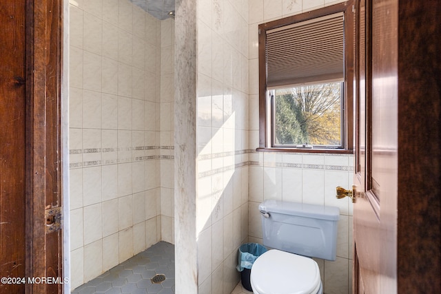 bathroom with tiled shower, toilet, and tile walls