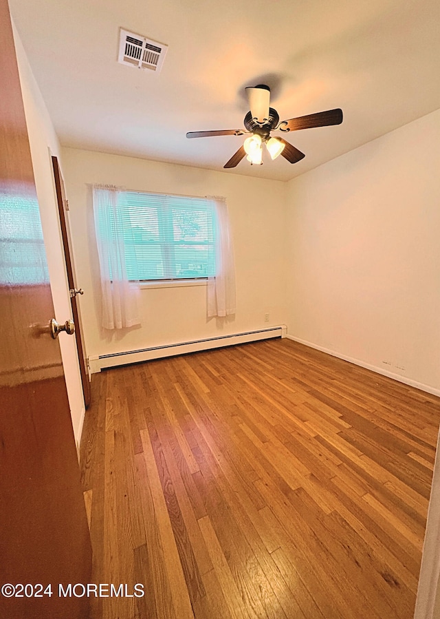 spare room featuring a baseboard heating unit, hardwood / wood-style floors, and ceiling fan