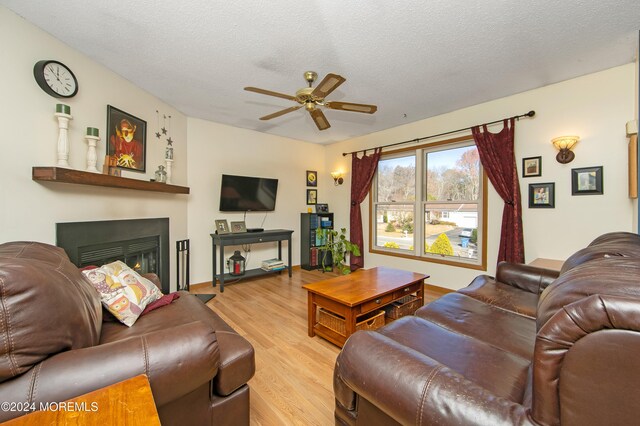 living room featuring light wood-type flooring, a textured ceiling, and ceiling fan