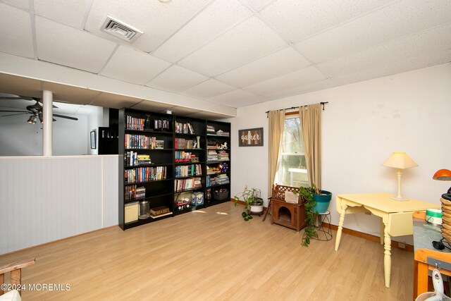 living area featuring a drop ceiling, hardwood / wood-style flooring, and ceiling fan