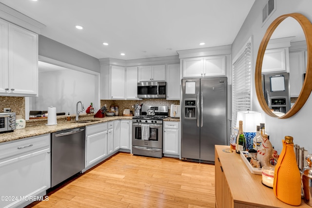 kitchen featuring sink, stainless steel appliances, decorative backsplash, white cabinets, and light wood-type flooring