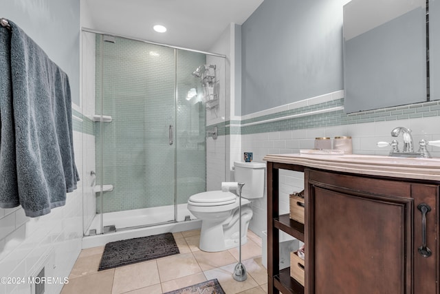 bathroom with tile patterned floors, toilet, a shower with door, vanity, and tile walls