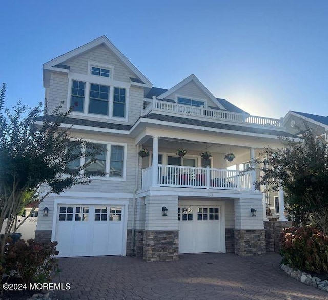 view of front of house featuring a balcony, stone siding, an attached garage, and decorative driveway