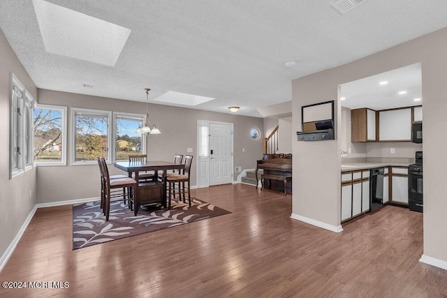 dining area featuring wood-type flooring, a textured ceiling, a skylight, and a notable chandelier