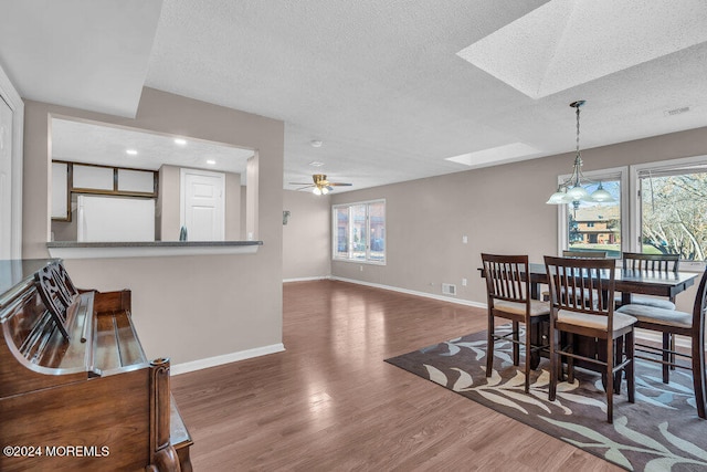 dining area with a textured ceiling, dark hardwood / wood-style flooring, a healthy amount of sunlight, and a skylight