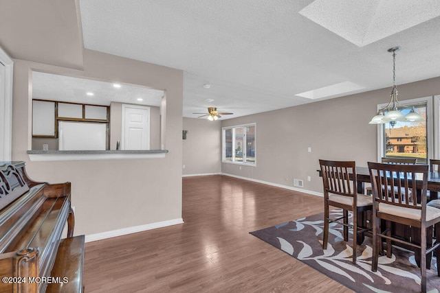 dining area with dark wood-type flooring, a skylight, a textured ceiling, and ceiling fan