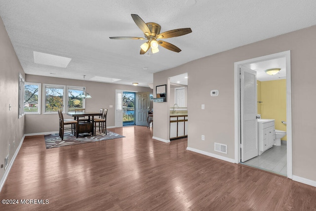 dining space featuring wood-type flooring, a textured ceiling, sink, ceiling fan, and a skylight