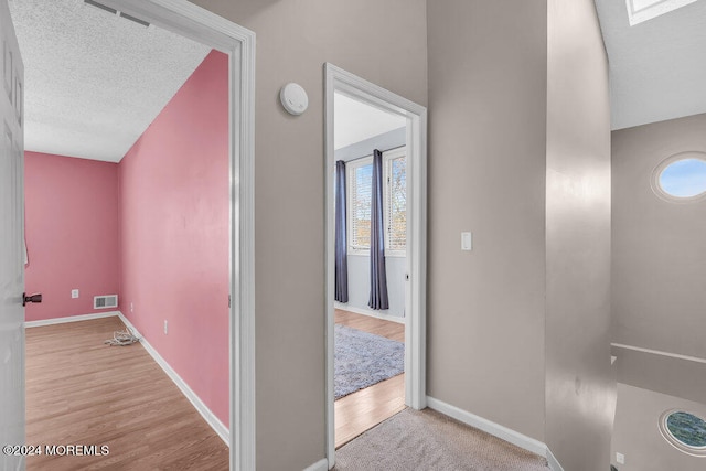 corridor with light wood-type flooring, a textured ceiling, and a healthy amount of sunlight