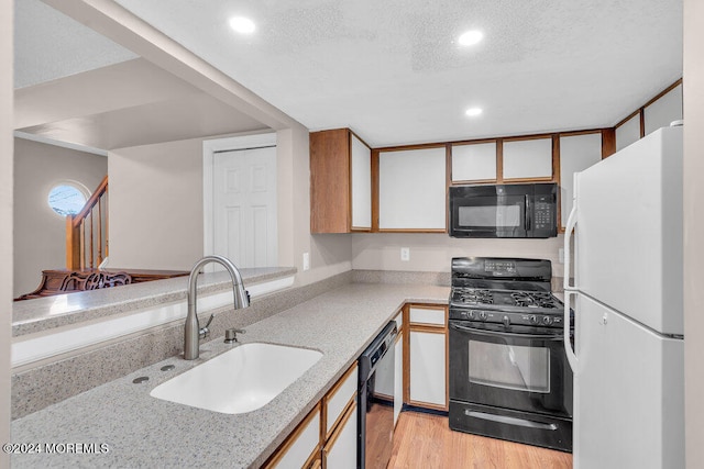 kitchen with light wood-type flooring, a textured ceiling, sink, and black appliances