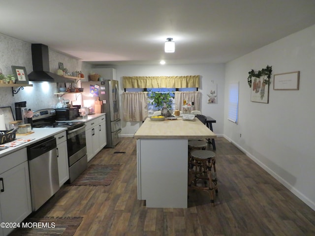 kitchen featuring appliances with stainless steel finishes, wall chimney exhaust hood, white cabinets, dark hardwood / wood-style floors, and a kitchen island