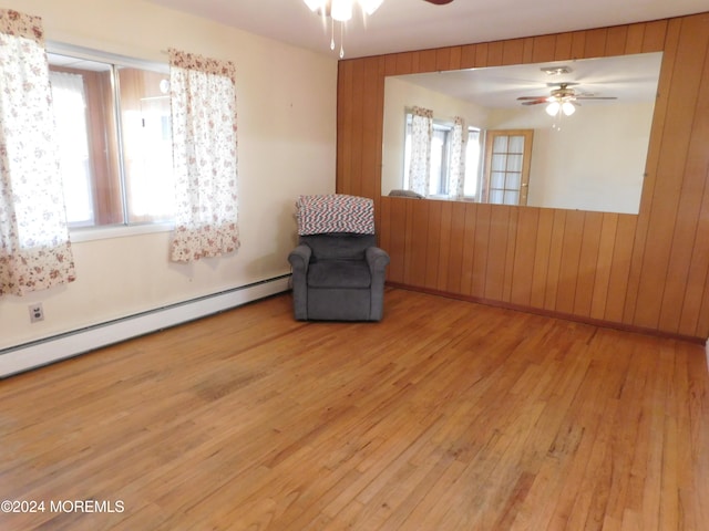 unfurnished room featuring baseboard heating, light wood-type flooring, wooden walls, and ceiling fan