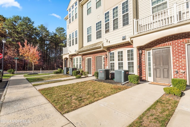 exterior space with central air condition unit, a balcony, and a yard