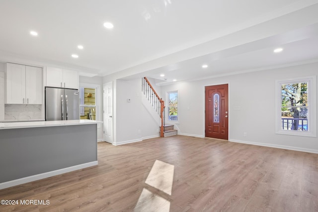 interior space featuring decorative backsplash, light hardwood / wood-style floors, white cabinetry, and stainless steel refrigerator