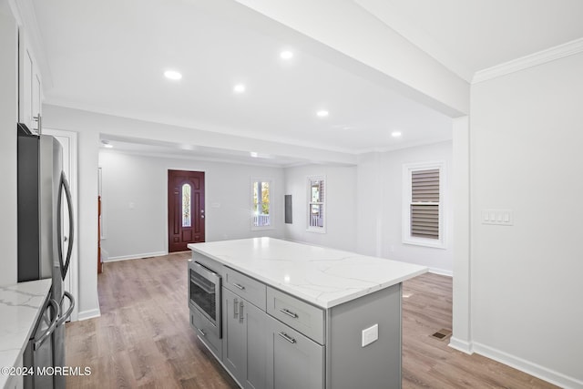 kitchen featuring stainless steel microwave, gray cabinetry, light stone countertops, and a center island