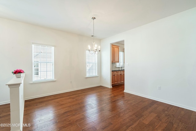 unfurnished dining area featuring a chandelier, dark wood-type flooring, baseboards, and a sink