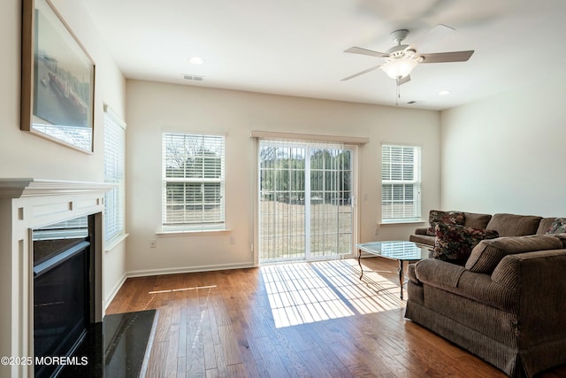 living room with visible vents, a fireplace with flush hearth, a healthy amount of sunlight, and hardwood / wood-style flooring