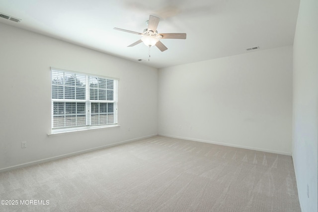 spare room featuring a ceiling fan, light colored carpet, and visible vents