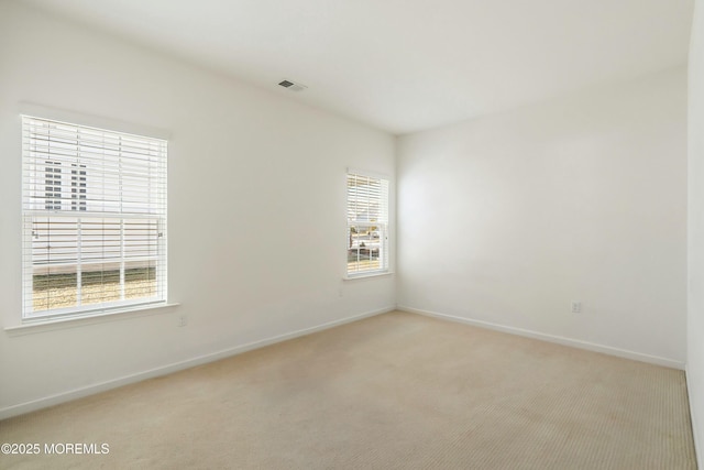 empty room with baseboards, visible vents, and light carpet