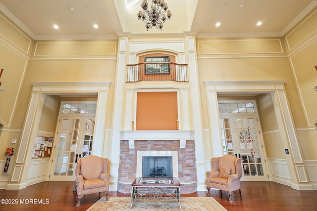 living area with french doors, a stone fireplace, wood finished floors, and a decorative wall