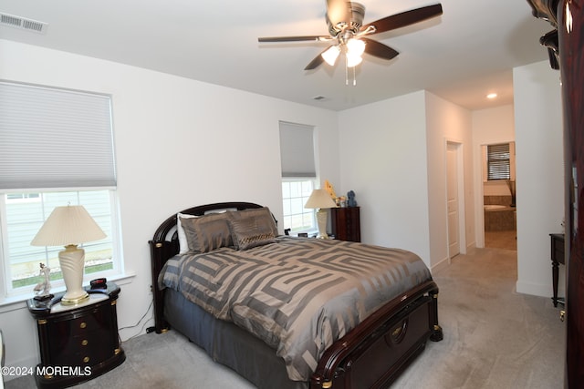 bedroom with ensuite bath, light colored carpet, multiple windows, and ceiling fan