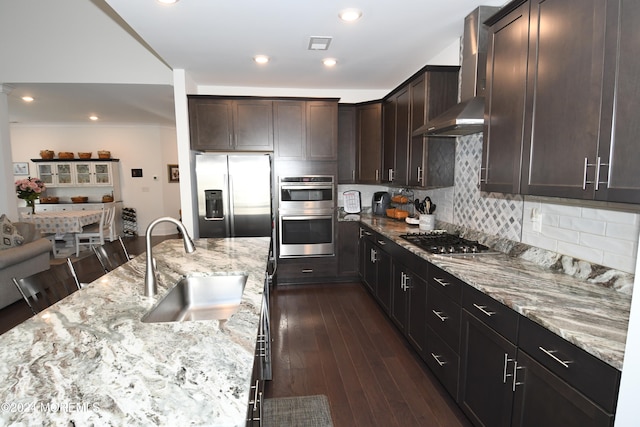 kitchen with appliances with stainless steel finishes, light stone countertops, sink, a breakfast bar, and wall chimney exhaust hood