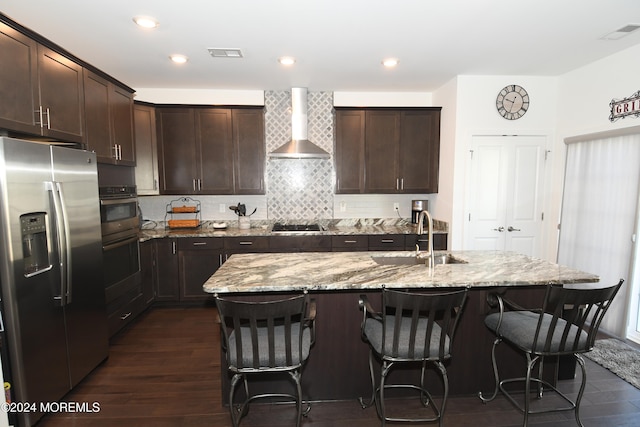 kitchen with stainless steel appliances, a center island with sink, sink, dark hardwood / wood-style floors, and wall chimney range hood