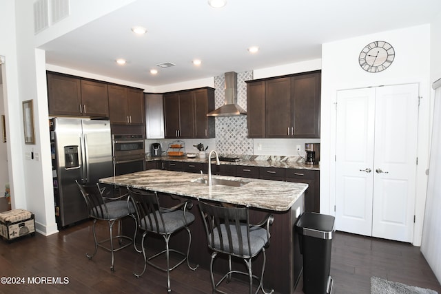 kitchen with a center island with sink, appliances with stainless steel finishes, dark hardwood / wood-style flooring, a breakfast bar area, and wall chimney exhaust hood