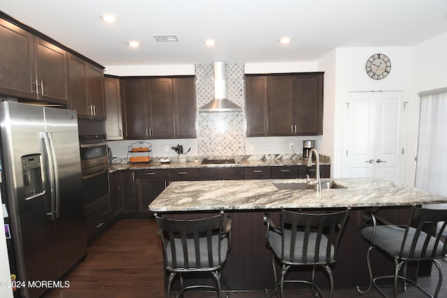 kitchen featuring a center island with sink, stainless steel appliances, wall chimney range hood, dark hardwood / wood-style floors, and sink