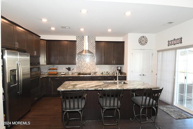 kitchen featuring stainless steel appliances, wall chimney exhaust hood, an island with sink, and sink