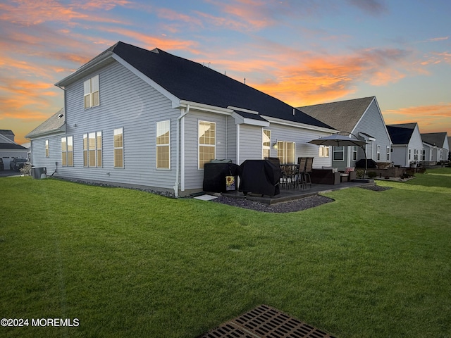 back house at dusk featuring central AC unit, a patio, and a lawn