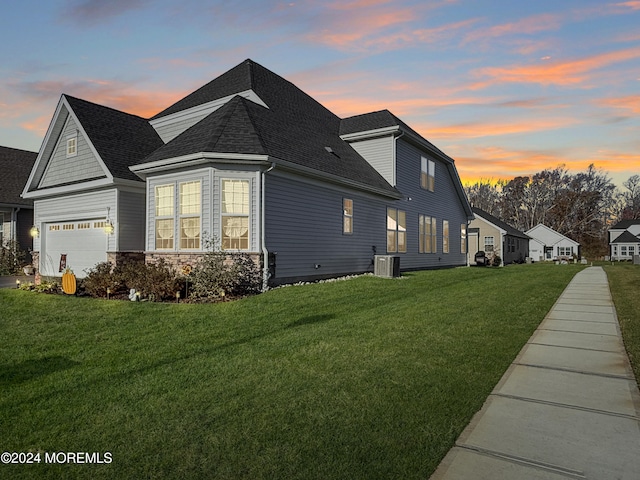 property exterior at dusk with a garage, central AC, and a yard