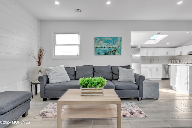 living room with a skylight, wooden walls, and sink