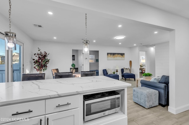 kitchen with white cabinets, decorative light fixtures, a healthy amount of sunlight, and light stone counters