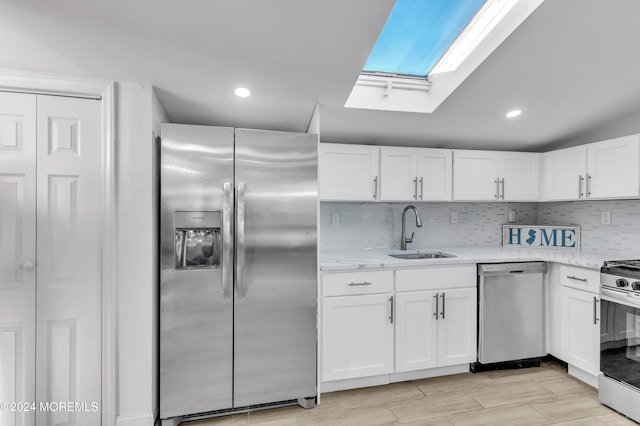 kitchen with white cabinets, vaulted ceiling with skylight, stainless steel appliances, and sink